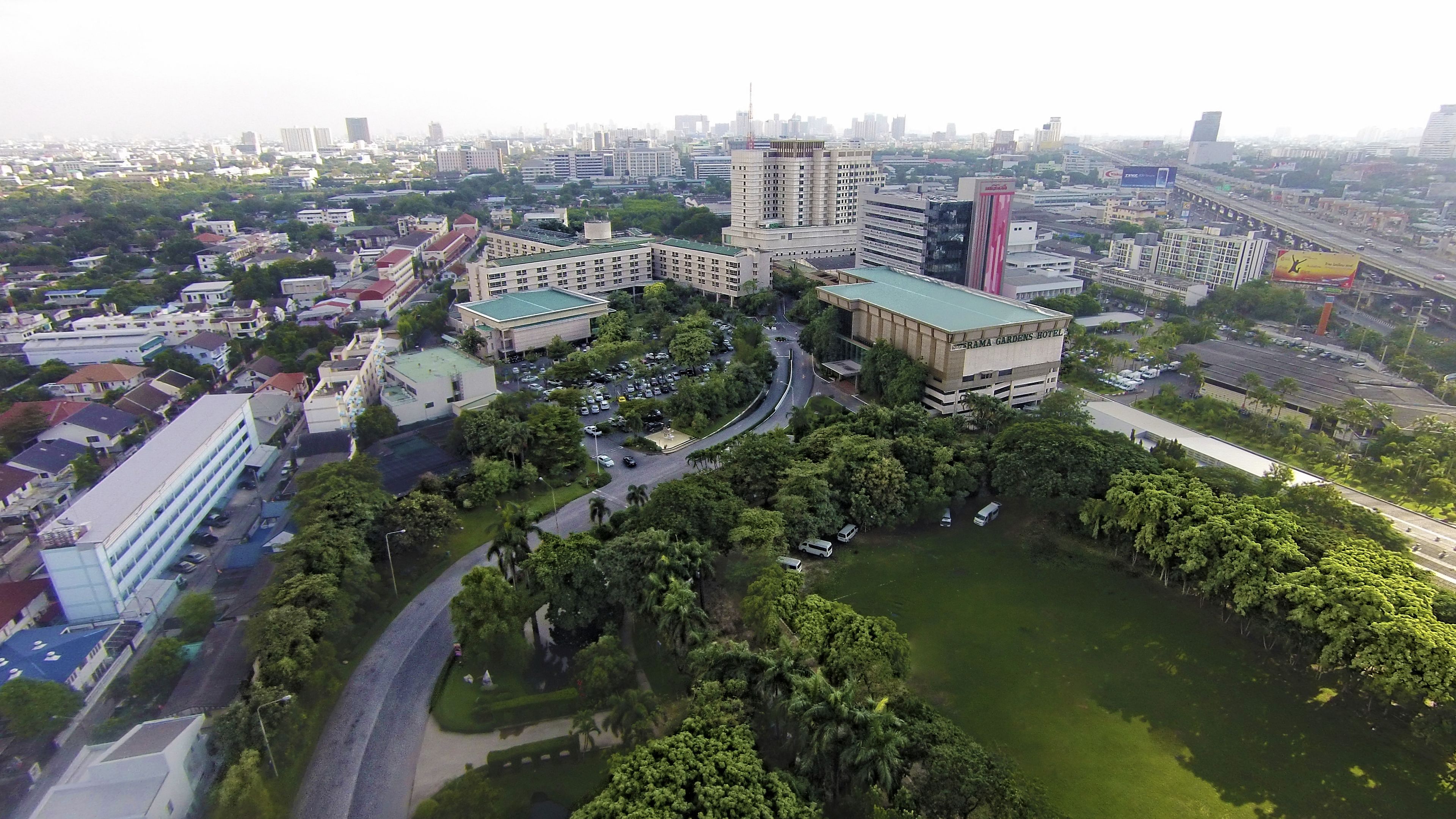 A large hotel with multiple buildings, surrounded by greenery and a parking area.