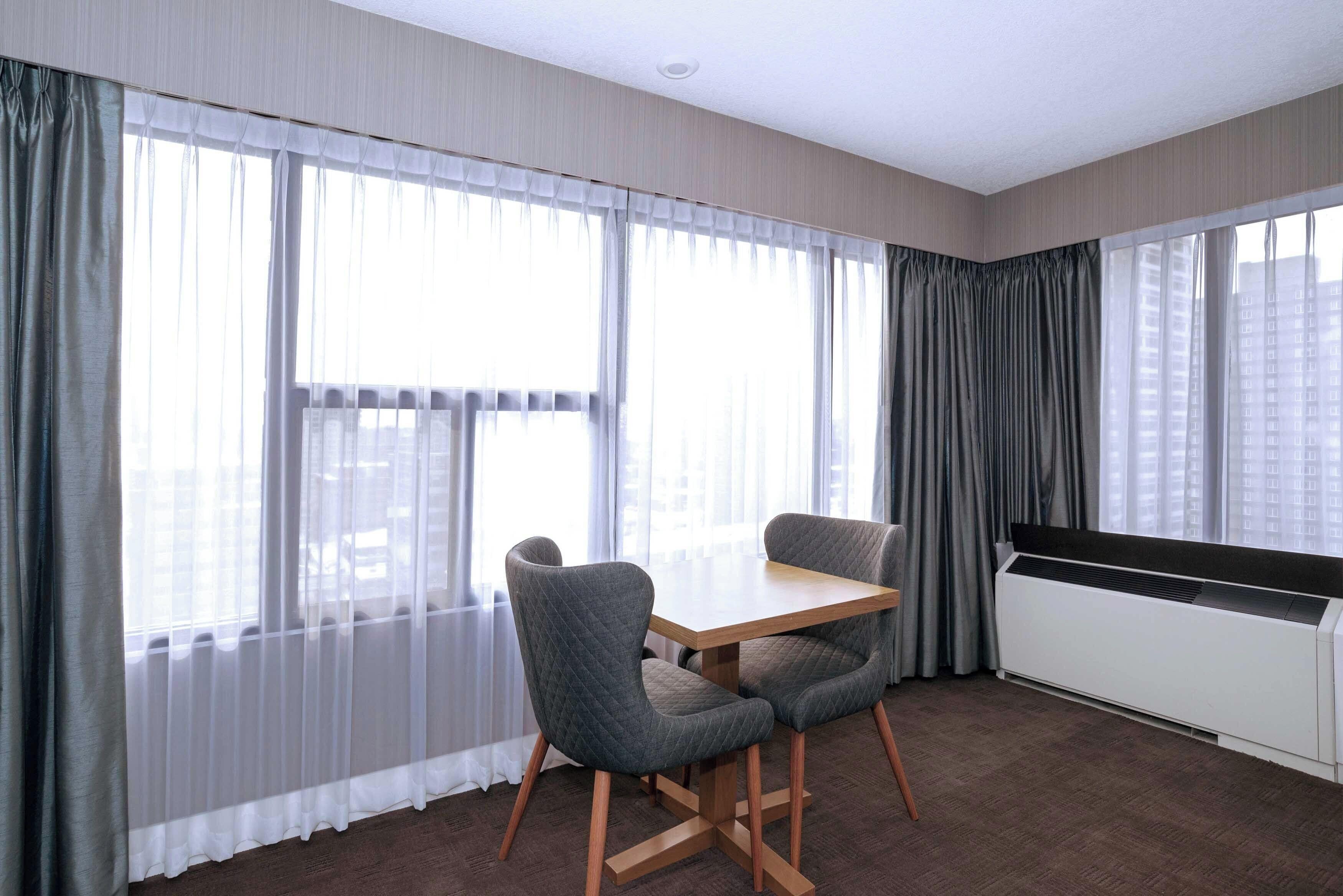 Una habitación con una mesa de comedor y sillas, ventanas amplias con cortinas y un radiador.
