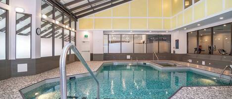 An indoor swimming pool with clear water, surrounded by a tiled floor and walls, and a ceiling with skylights.