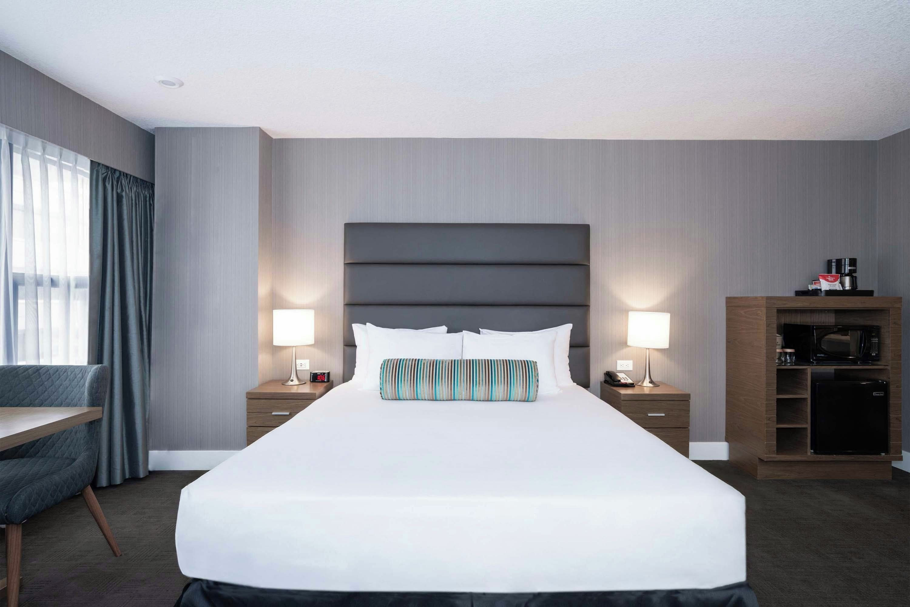 A hotel room with a large bed, bedside lamps, a desk, and a minibar.