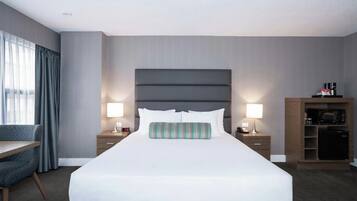 Una habitación de hotel con una cama grande, lámparas de noche, un escritorio y un minibar.