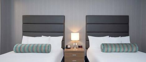 Een hotelkamer met twee bedden, een nachtkastje met een lamp en een klein lade.