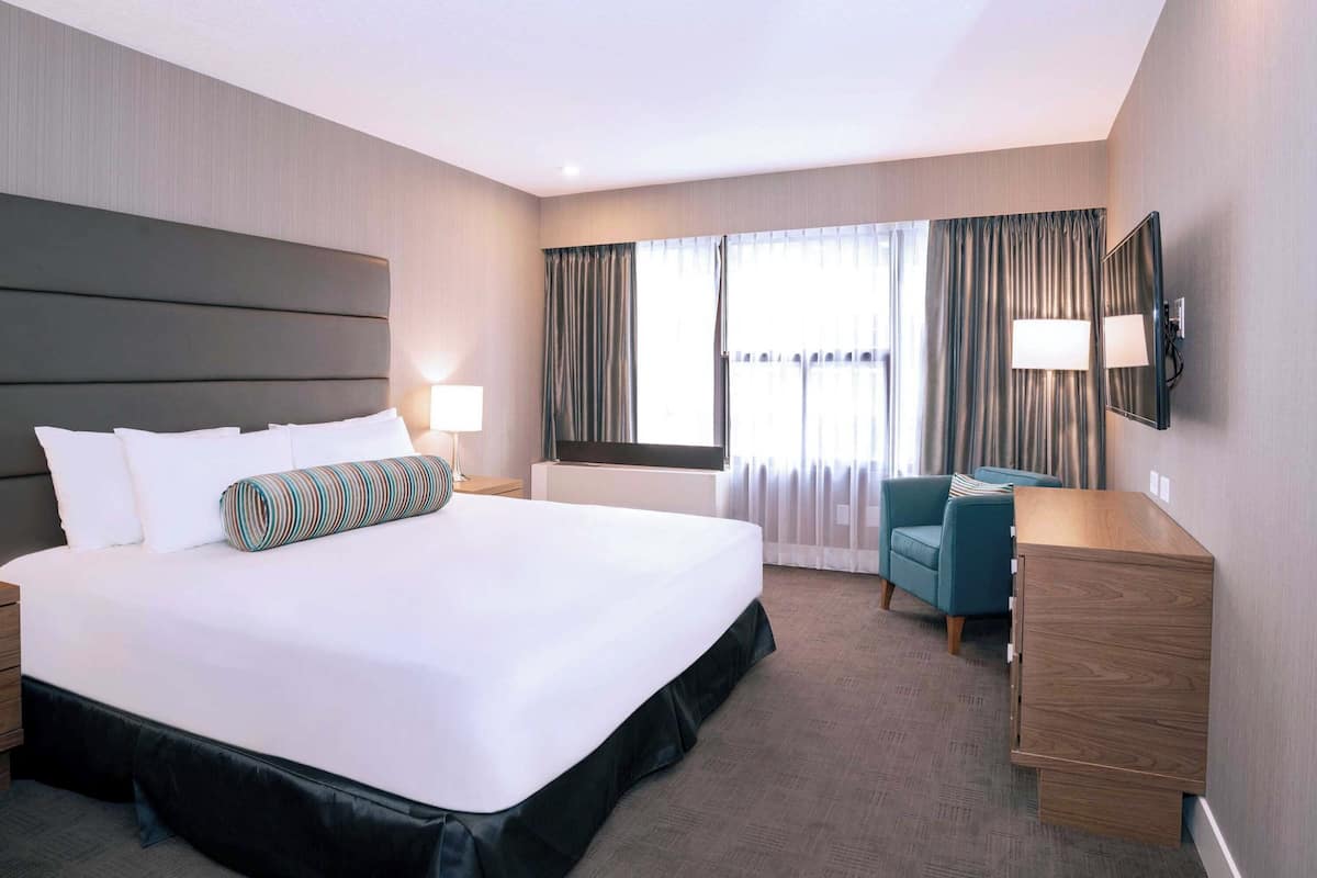 Una habitación de hotel con una cama grande, un escritorio, una silla, un televisor y una ventana con cortinas.