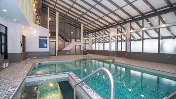 An indoor swimming pool with clear water, a safety sign, and a glass ceiling.