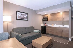 A compact living space with a sofa, a coffee table, a framed picture on the wall, a microwave, and a refrigerator.