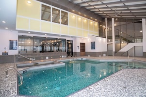 Una piscina interior con agua cristalina, rodeada por un suelo de baldosas con indicaciones de profundidad.