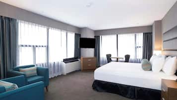 A hotel room with a bed, a desk, a chair, a TV, and a window with curtains.