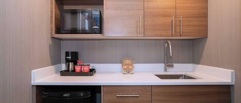 A modern kitchen with wooden cabinets, a built-in microwave, a coffee machine, and a dishwasher.