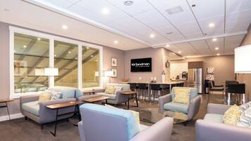 A hotel lobby with seating areas, a TV screen, and a kitchen area.