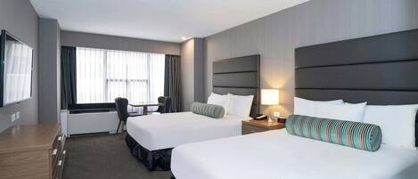 A hotel room with two beds, a desk, a chair, and a large window with curtains.