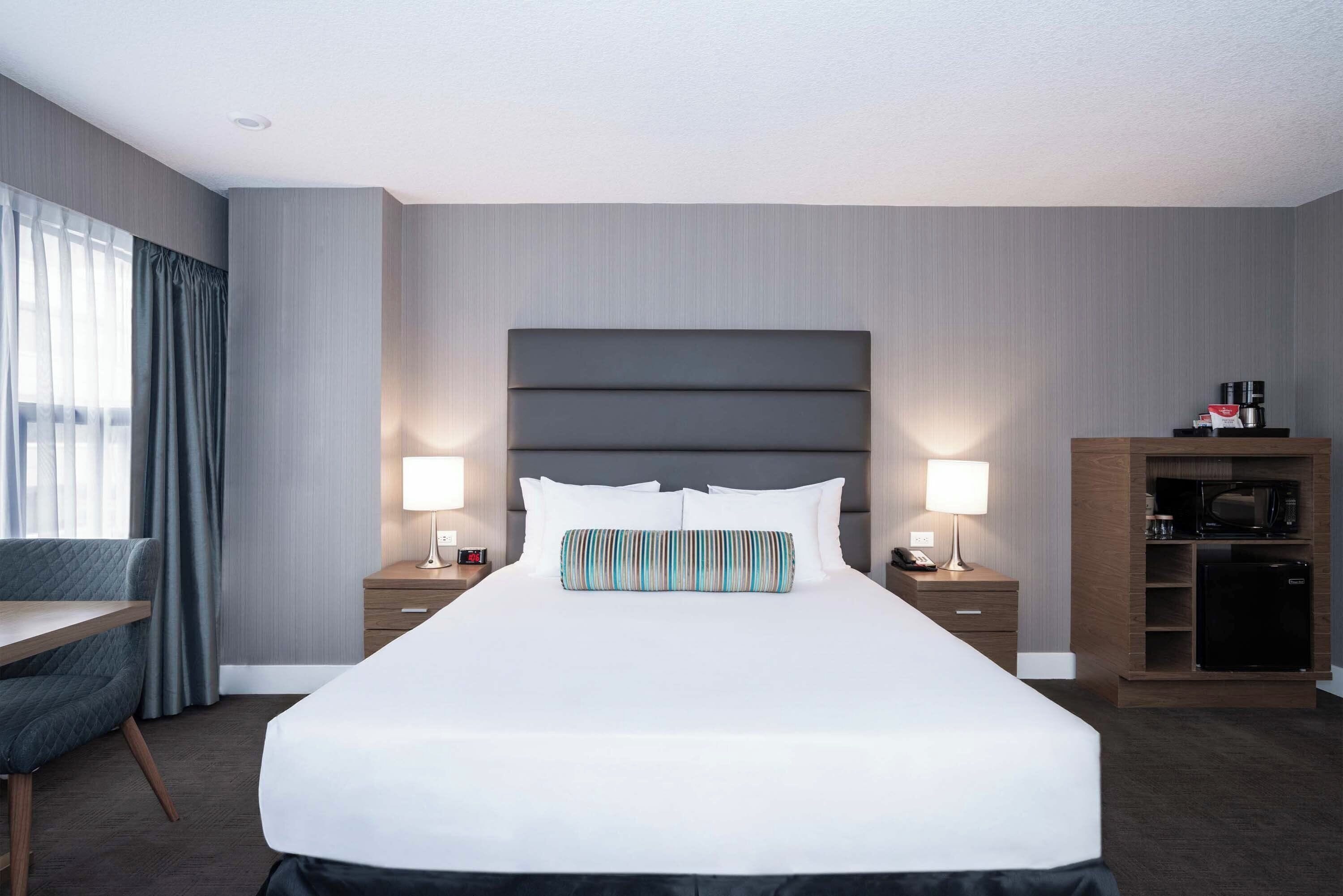 Habitación de hotel con una cama grande, mesitas de noche con lámparas, un escritorio, una silla y un microondas integrado.