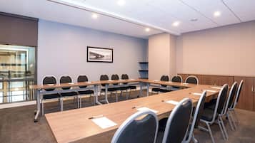Un salón de conferencias con una larga mesa, sillas y un cuadro en la pared.
