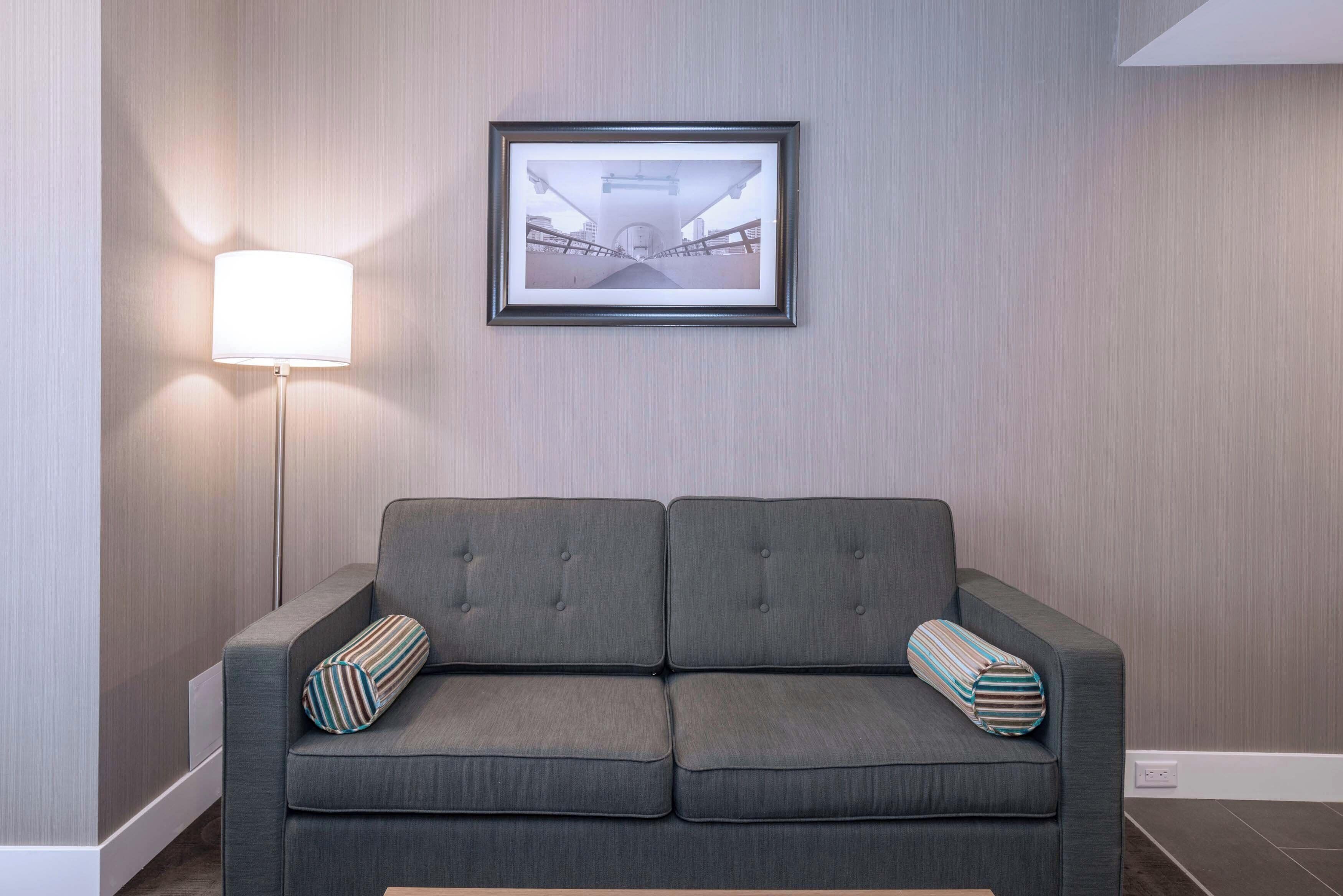 Un sofá gris con almohadones a rayas y un cuadro en la pared.