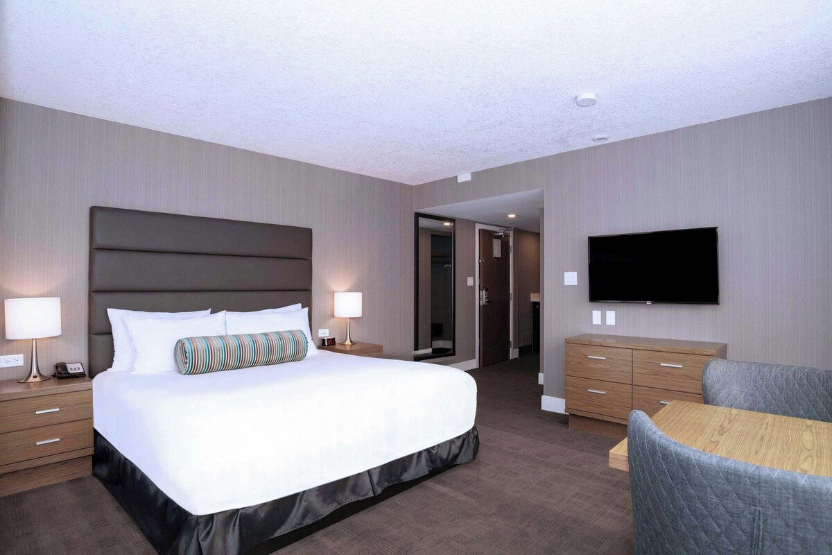A hotel room with a large bed, bedside tables, a TV, and a seating area.