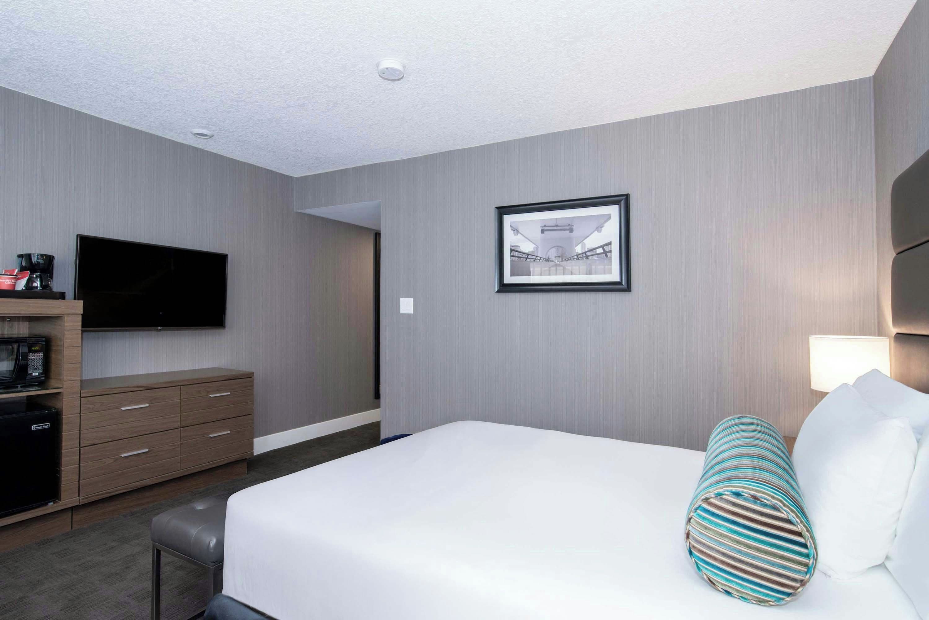 Una habitación de hotel con una cama, televisor, cafetera y un cuadro en la pared.