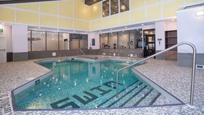 An indoor swimming pool with clear water, tiled floor, and a metal handrail.