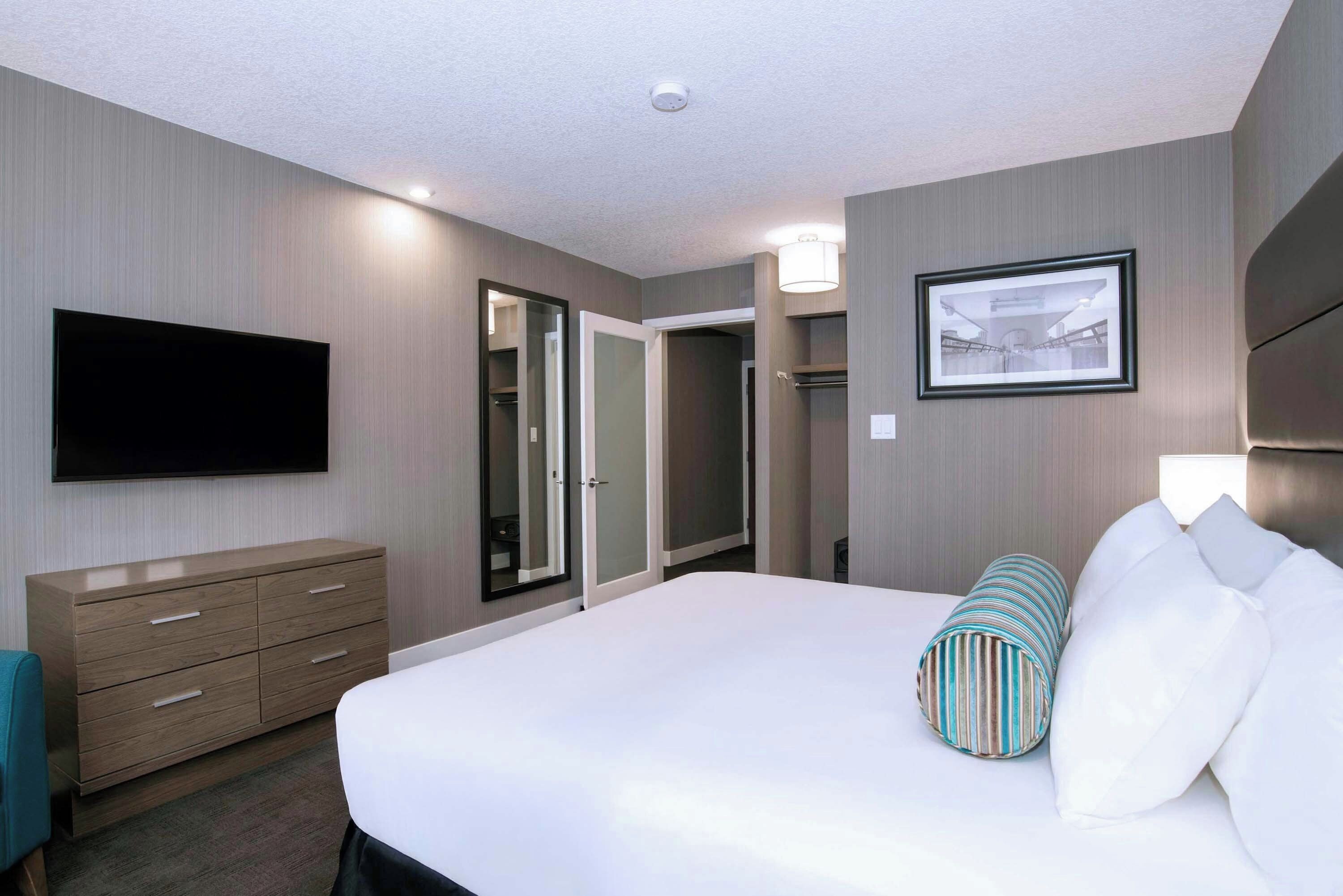 Habitación de hotel con cama, televisión de pantalla plana, cómoda, espejo y un cuadro en la pared.