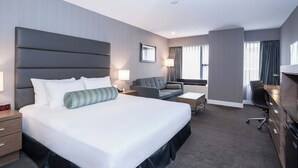 A modern hotel room with a large bed, a desk, a sofa, and a chair.