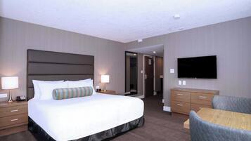 A hotel room with a large bed, bedside tables with lamps, a flat-screen TV mounted on the wall, a wooden dresser, and a small table with a chair.