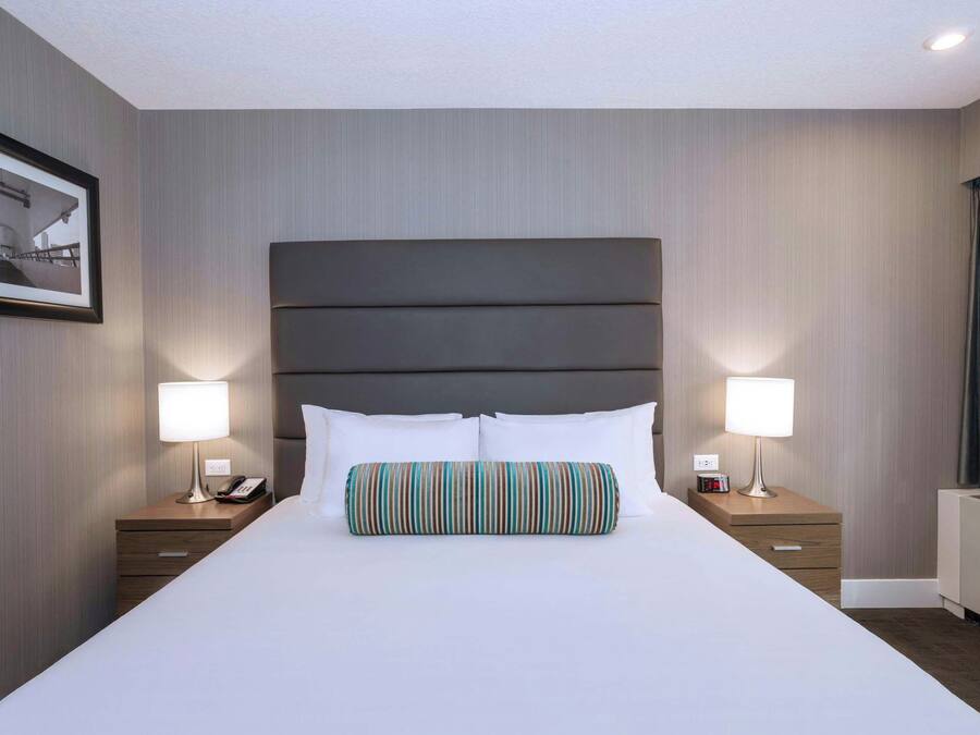 Quarto de hotel com cama grande, duas mesas de cabeceira, encosto de cama e quadro na parede.