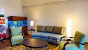 A hotel room with a sofa, two armchairs, a small table, a lamp, and a fish tank.