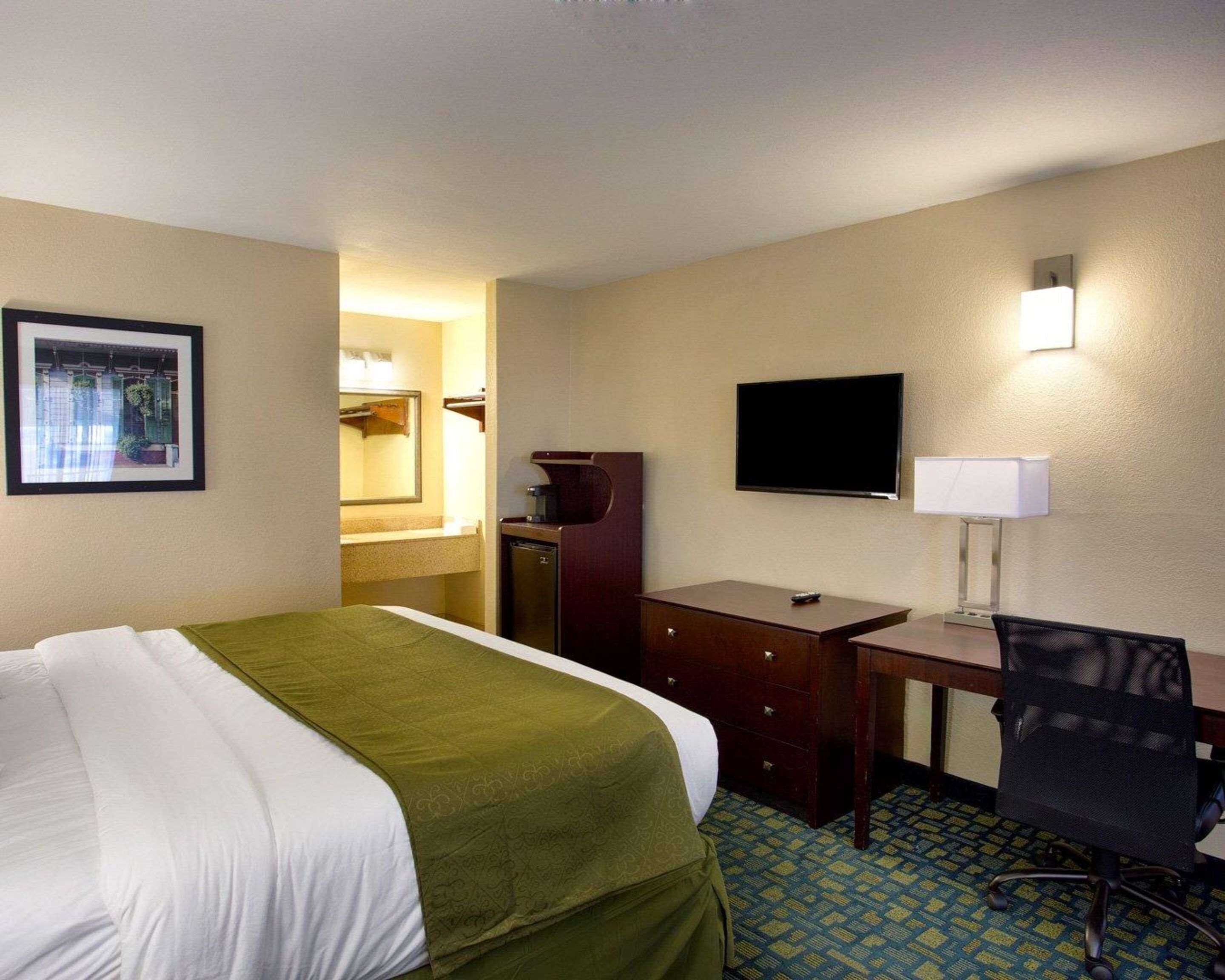 A hotel room with a bed, a desk, a chair, a television, a mirror, and a framed picture on the wall.