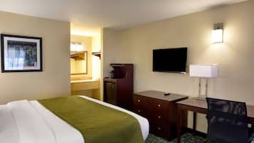 Une chambre d’hôtel comprenant un lit, un bureau, une chaise, une télévision, un miroir et un tableau encadré accroché au mur.