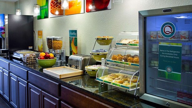 A breakfast buffet with various food items, a refrigerator with a sign indicating items are available only during breakfast hours, and a wall with fruit and vegetable images.