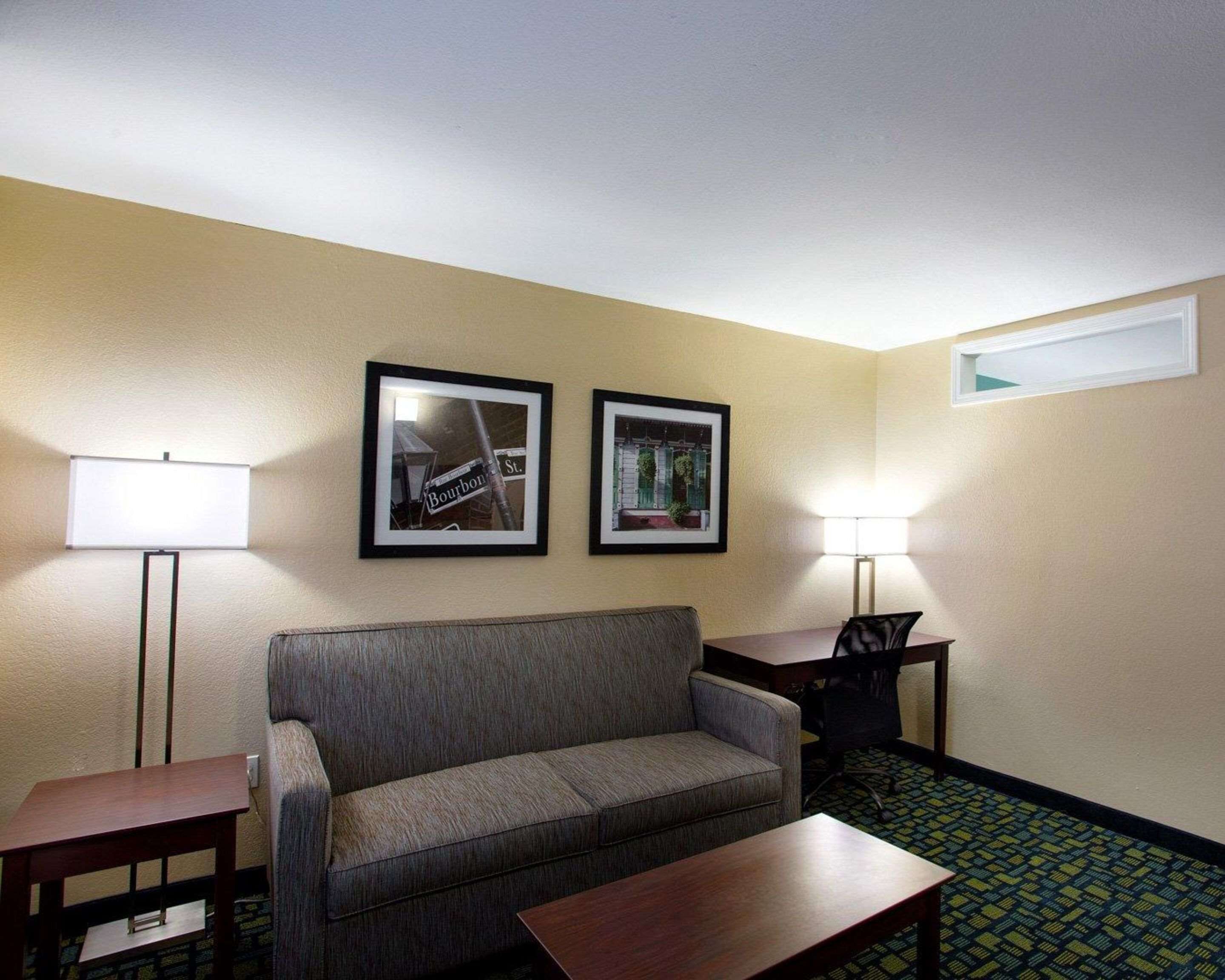 A hotel room with a sofa, a small table, two framed pictures on the wall, and a lamp on either side of the sofa.
