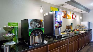 Un buffet de petit-déjeuner en libre-service avec des distributeurs de café et de jus de fruits, un panneau indiquant que les produits sont frais, et une grande variété d’aliments.