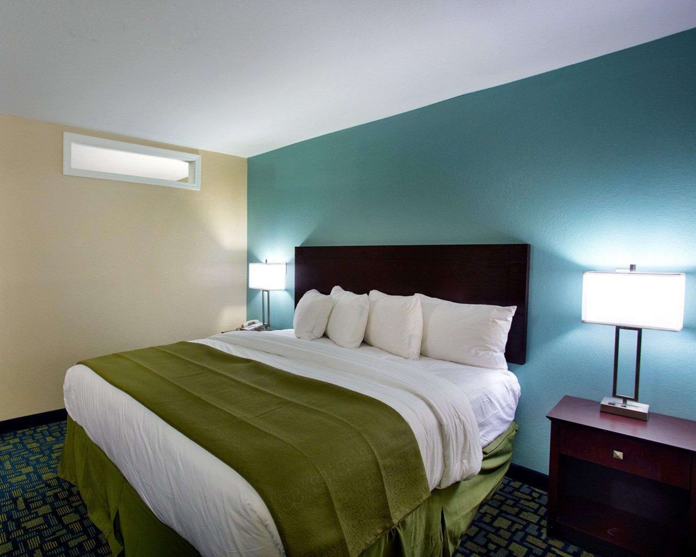 A hotel room with a large bed, a nightstand, a lamp, and a wall-mounted light fixture.