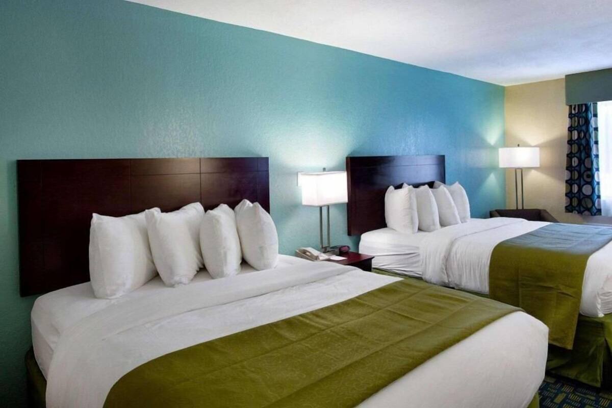 A hotel room with two beds, a green bedspread, and a teal wall.