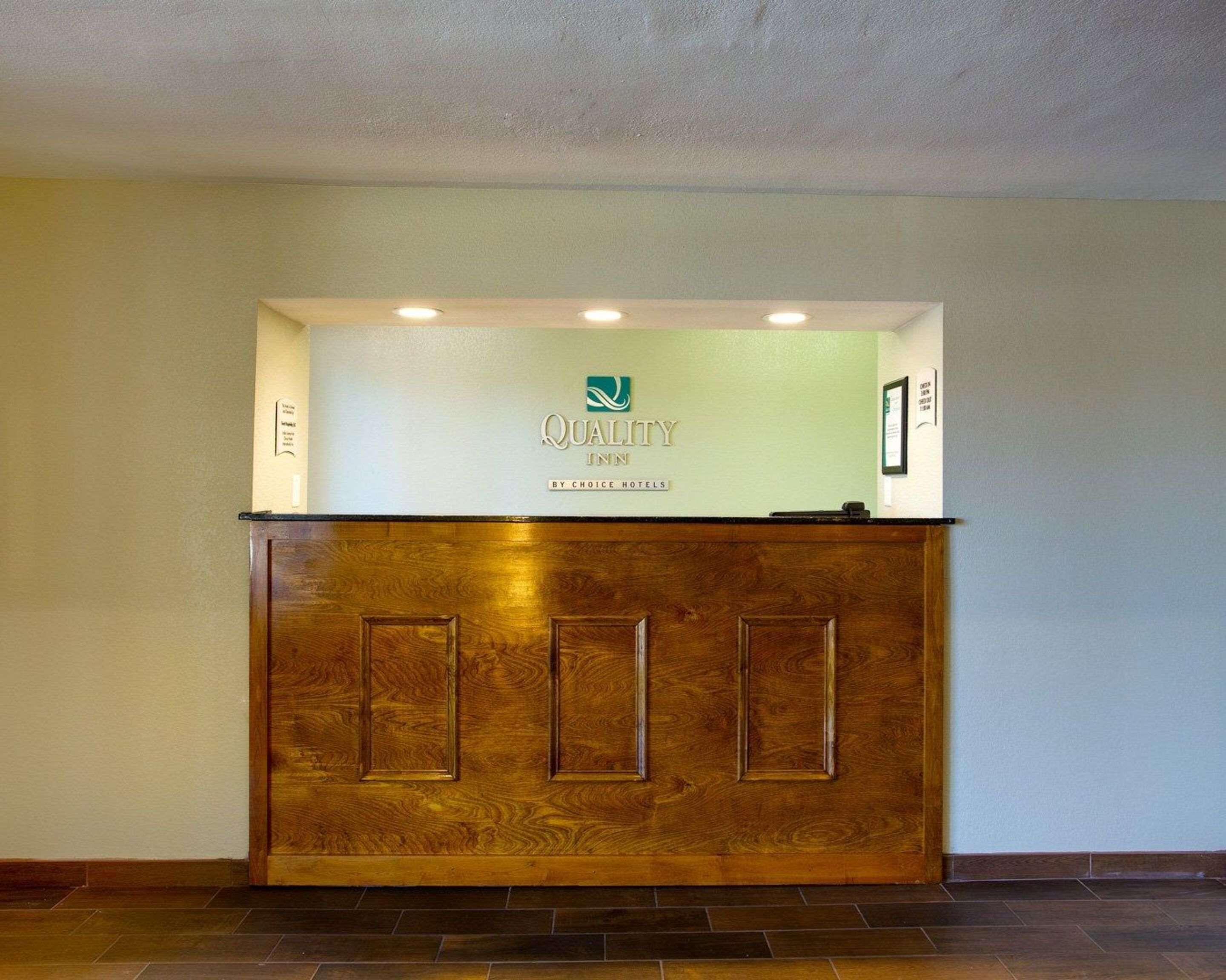 Un mostrador de recepción con detalles de madera, un logotipo y un cartel que indica que es un Quality Inn de Choice Hotels.