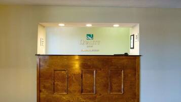 Un mostrador de recepción con detalles de madera, un logotipo y un cartel que indica que es un Quality Inn de Choice Hotels.