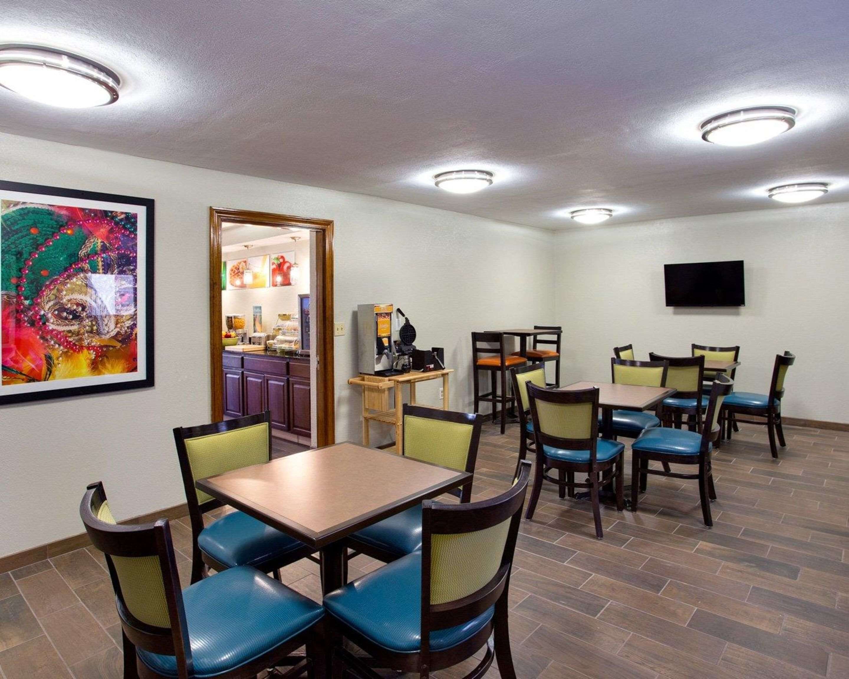 Un espace repas avec des tables et des chaises, une cuisine à l’arrière-plan et un téléviseur accroché au mur.