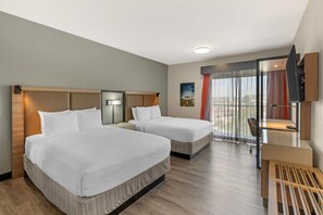 Habitación de hotel con dos camas, un escritorio, un televisor y un ventanal con cortinas.