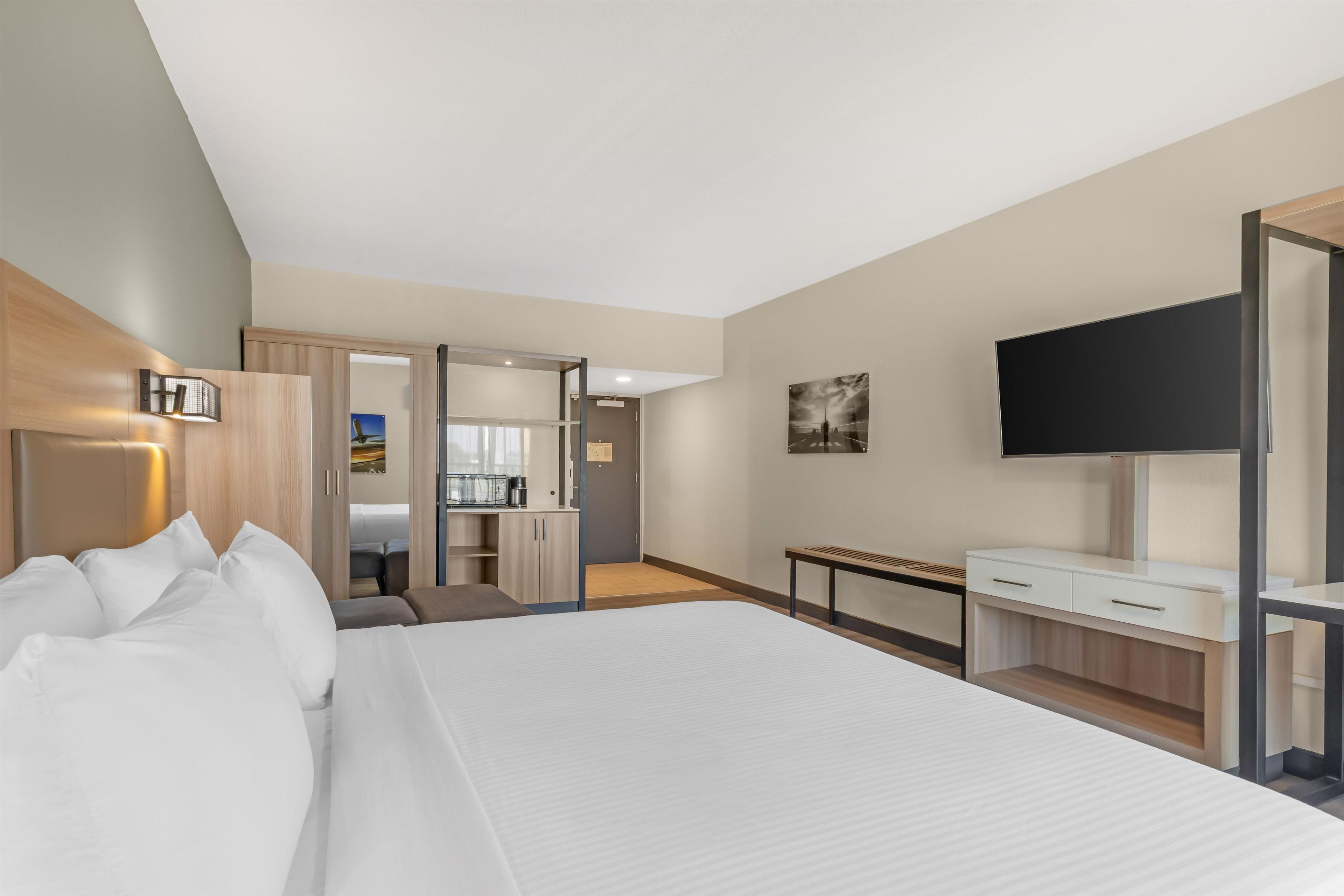 A modern hotel room with a large bed, a desk, a TV, and a wardrobe.