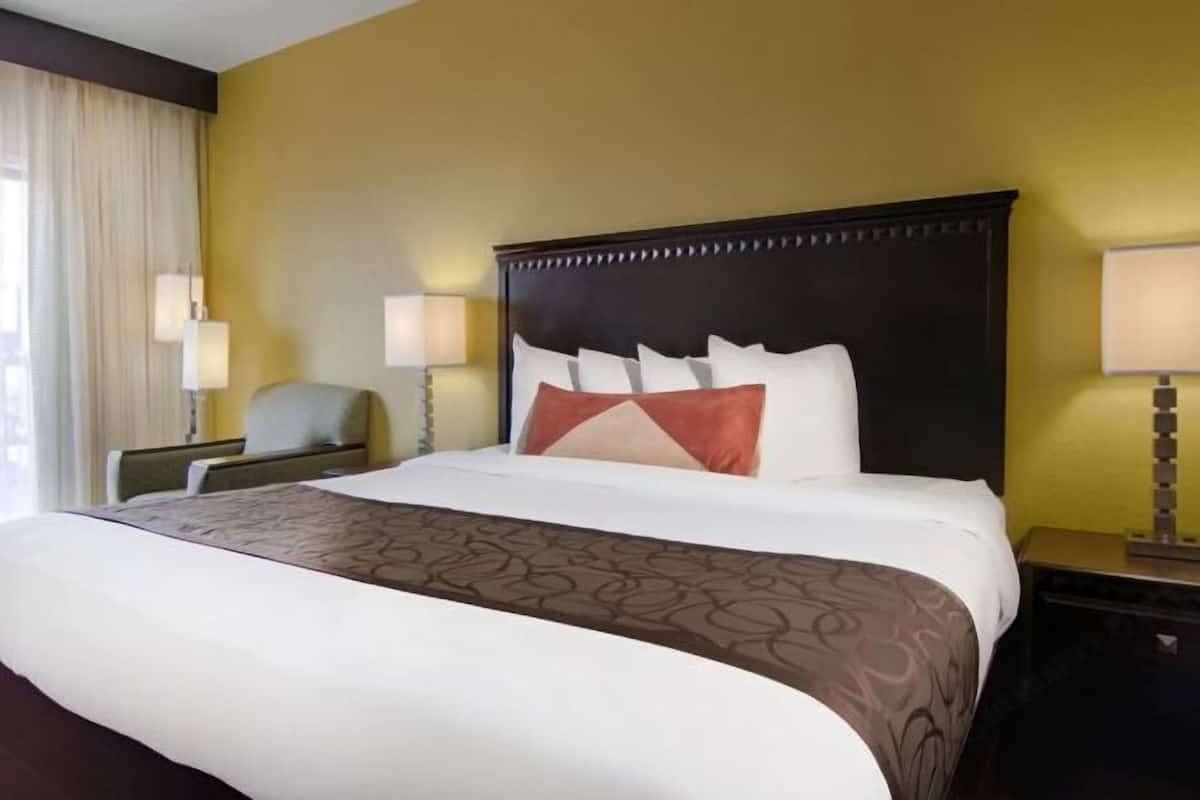 A hotel room with a large bed, two bedside lamps, a chair, and a nightstand.