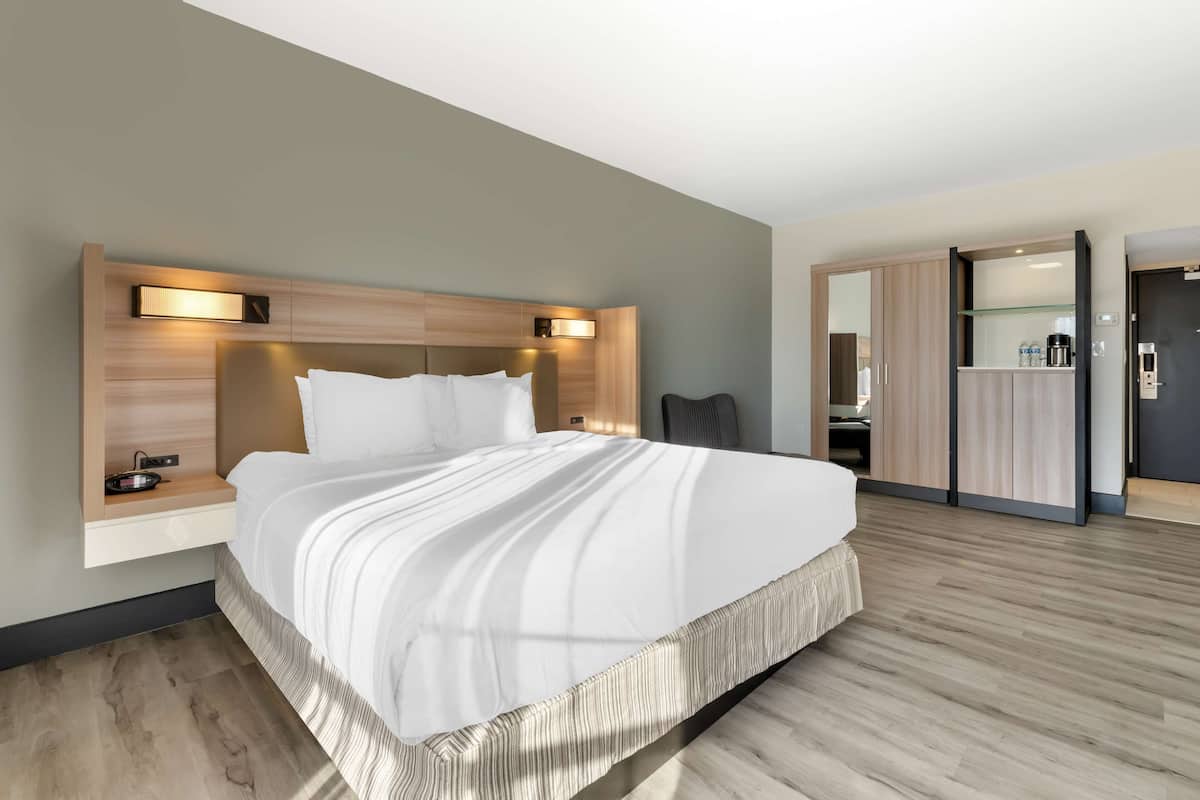 A modern hotel room with a large bed, bedside tables, and built-in lighting.