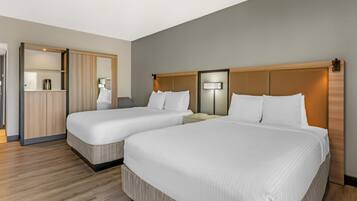 A hotel room with two beds, a wardrobe, and a nightstand with a lamp.