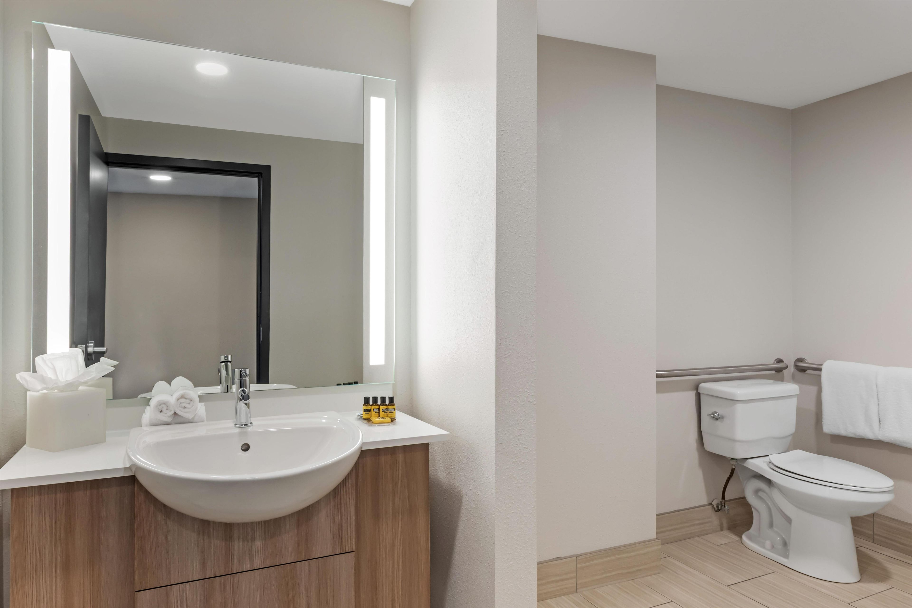 Un baño moderno con un espejo grande, un lavabo y un inodoro.
