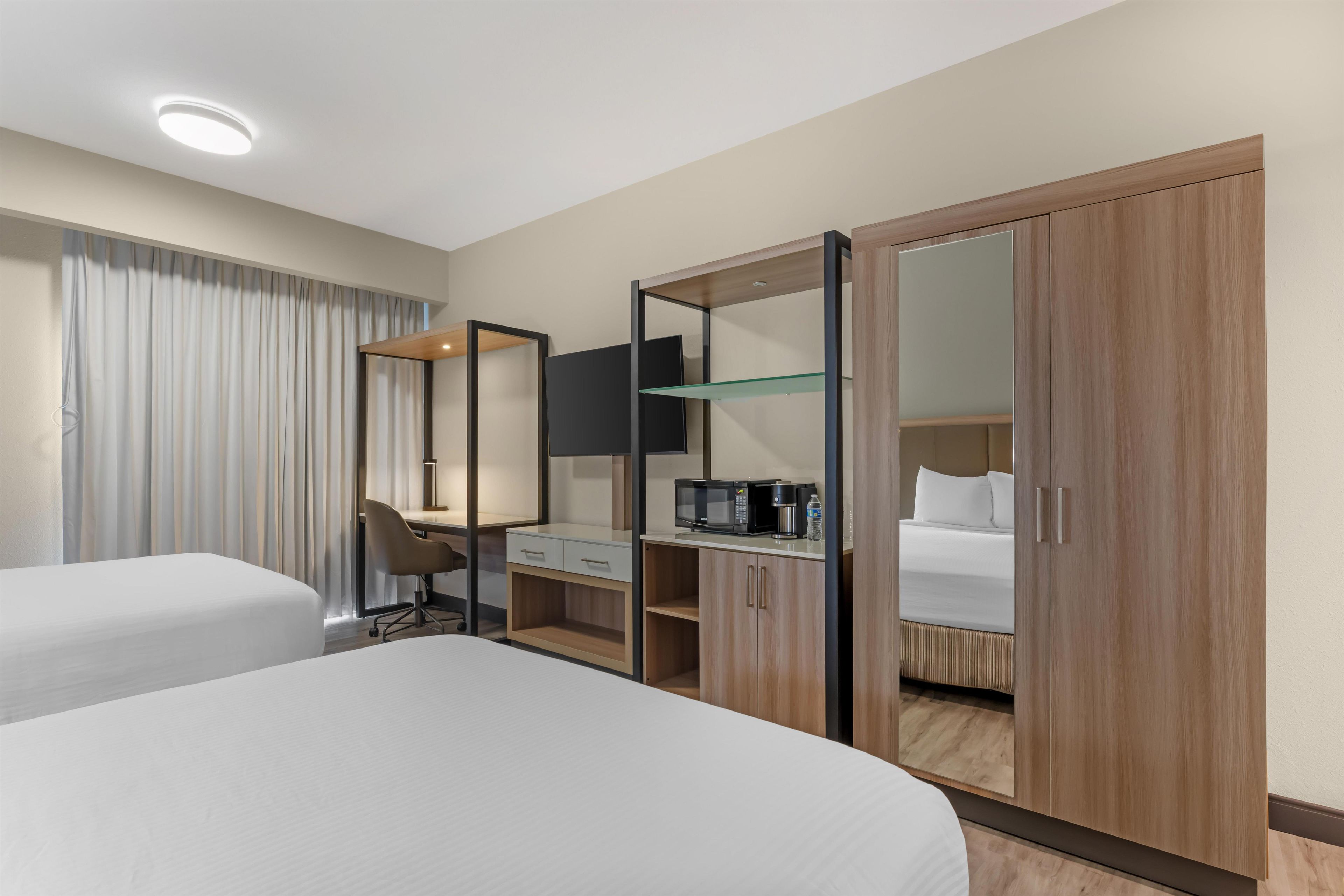 Ein Hotelzimmer mit zwei Betten, einem Schreibtisch, einem Kleiderschrank und einem Spiegel.
