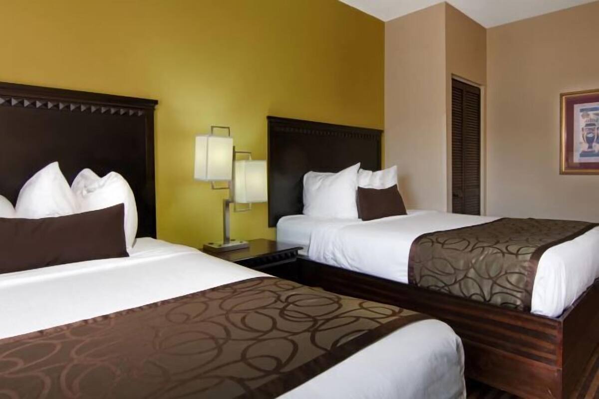 A hotel room with two beds, a nightstand, a lamp, and a framed picture on the wall.