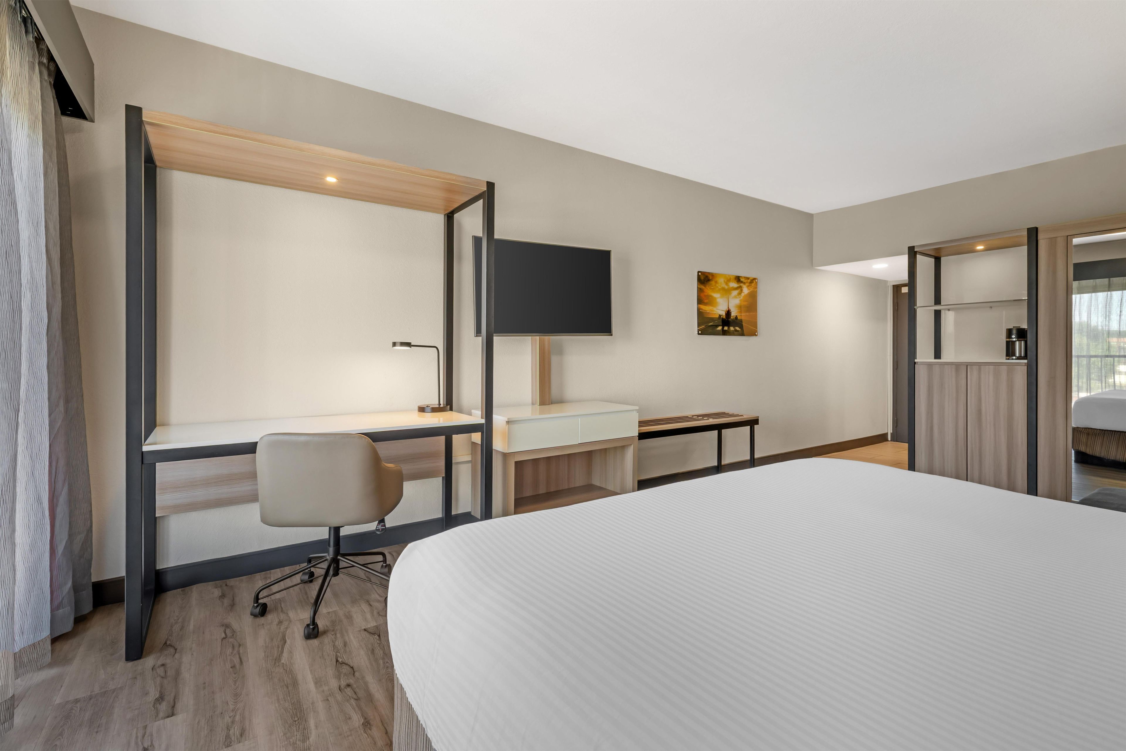 A hotel room with a large bed, a desk with a chair, a television, and a painting on the wall.