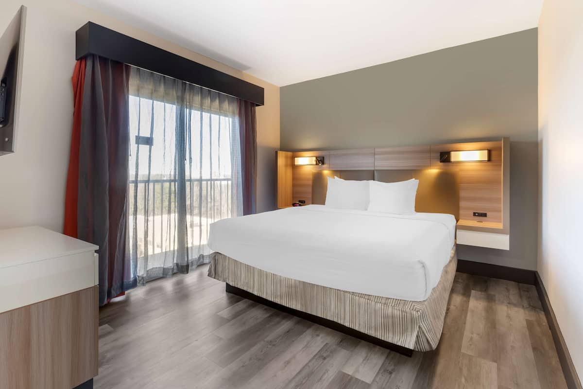A modern hotel room with a large bed, a bedside table, and a window with curtains.
