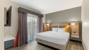 A hotel room with a bed, a TV mounted on the wall, a window with curtains, and a bedside table.