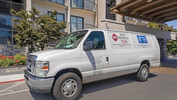 A white van parked in front of a building with balconies and a covered walkway.