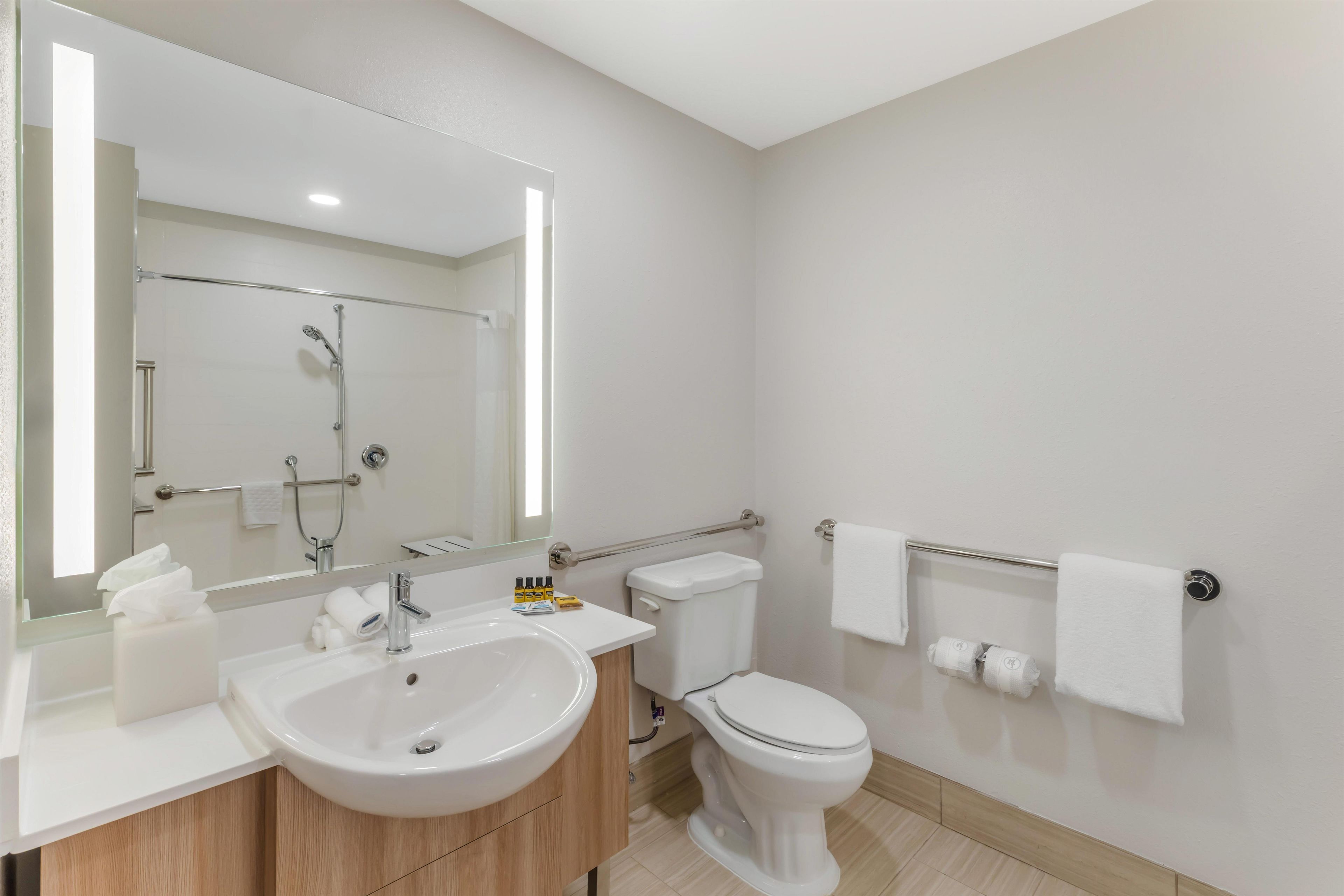 Un baño moderno con un espejo grande, un lavabo, un inodoro y una ducha.