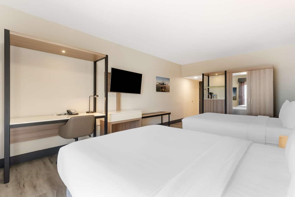 A hotel room with two beds, a desk, a chair, a TV, and a small table.