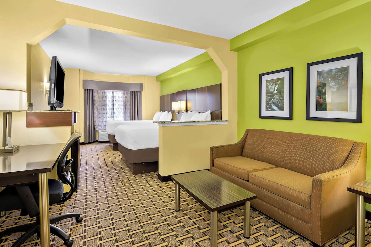 A hotel room with a bed, a sofa, a desk, a chair, a TV, and framed pictures on the wall.